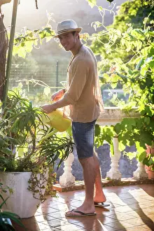 Wachsend Prints: Young man watering plants in garden Side view of young stylish man watering plants in garden in sunlight