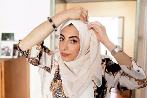 Adjusting Prints: Young muslim woman putting on hijab headscarf