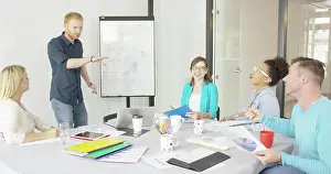 Conversation Prints: Young people in office sharing ideas Cheerful coworkers in casual clothing sitting around desktop in conference hall