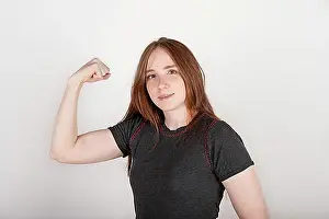 Thirty Prints: Young red-haired woman proudly showing her bicep. Concept of feminism, girl power