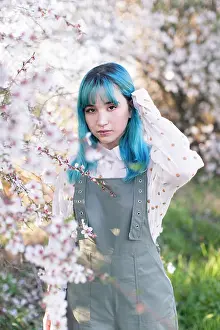 Individuality Prints: Young stylish female with long blue hair looking at camera wearing trendy overall enjoying blooming tree while standing