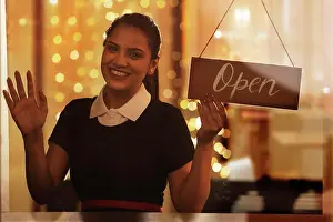 Exhilaration Prints: A YOUNG WAITRESS HAPPILY LOOKING AT CAMERA WHILE HOLDING OPEN SIGN BOARD