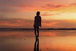 Glow Prints: Young woman with arms raised facing colorful sunset at low tide beach