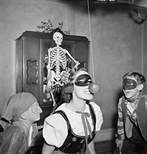 Effort Prints: Young woman attempting to bite apple while two boys are watching during Halloween