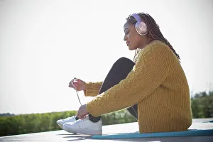 Sweater Prints: Young woman with headphones tying shoelace outdoors
