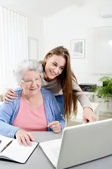 White Hair Prints: Young woman helping old senior woman doing paperwork and administrative procedures with laptop computer at home