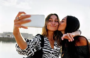 Messaging Prints: Young woman kissing friend while taking selfie against clear sky