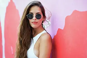 Vivid Prints: Young woman with long hair wearing stylish sunglasses and standing near red building wall in city