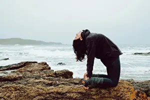 Fast Prints: young woman with meditating practicing yoga and sitting on rocks near sea