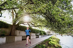 Runner Prints: Young woman runs on paved path through a tree tunnel next to river