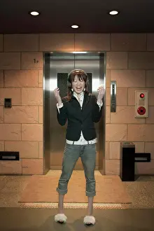 Spotlight Prints: Young woman standing in front of elevator wearing headphones and laughing, Tokyo, Japan
