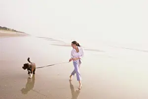 Adult Animal Prints: Young woman taking her dog for a walk on the beach