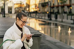 Jeans Prints: Young woman using smart phone while sitting on bench in city