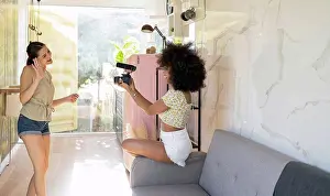 20 To 25 Years Prints: Young woman waving in camera held by afro female friend while filming at home