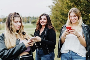 Small Group Of People Prints: Three young women using their phones in park